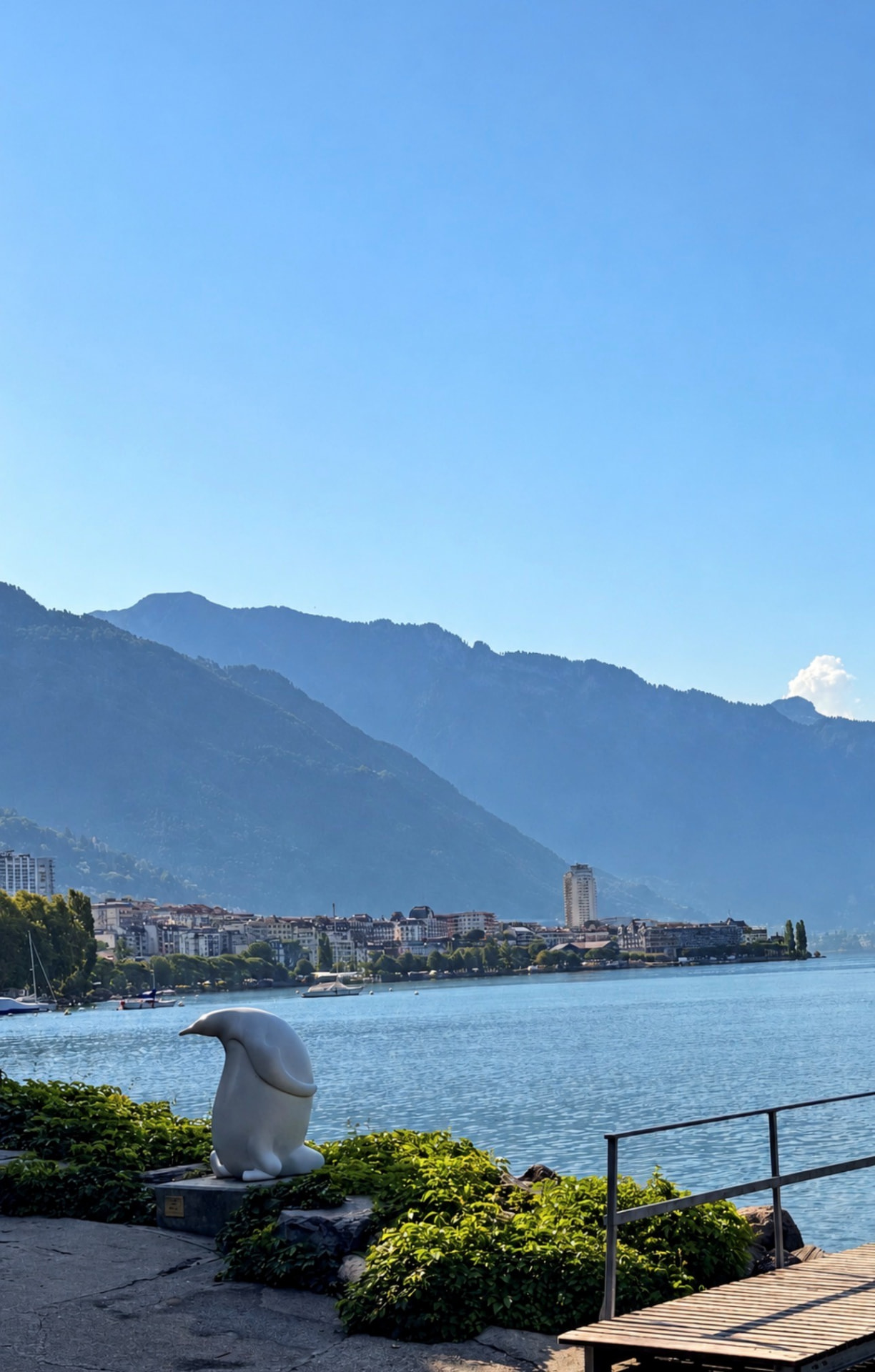The Montreux promenade with a white lakeside sculpture, the town of Montreux and the Alps beyond